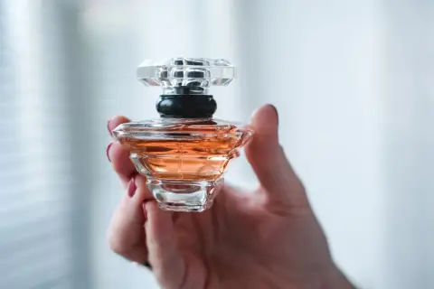 Dłoń trzyma flakonik perfum o bursztynowym kolorze, przypominający Baccarat Rouge.